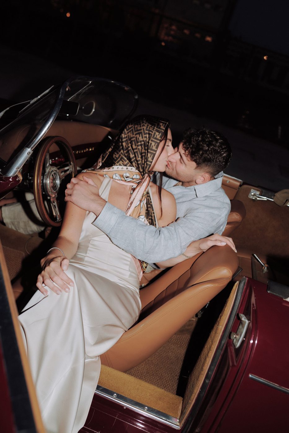 The couple kissing in a vintage car at night